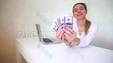 年轻女子坐在桌子旁，手提着<strong>银色笔记本</strong>电脑，拿着相机演示着钱